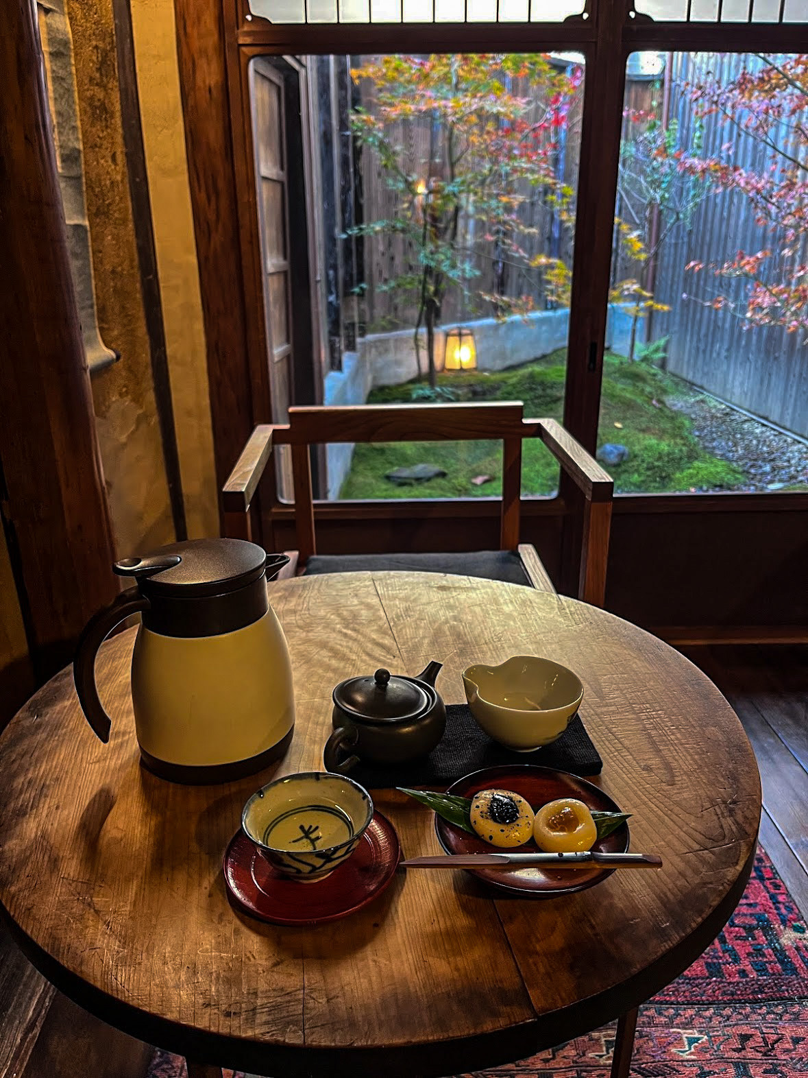 Tea vessels and small dishes on a wooden table beside a garden window